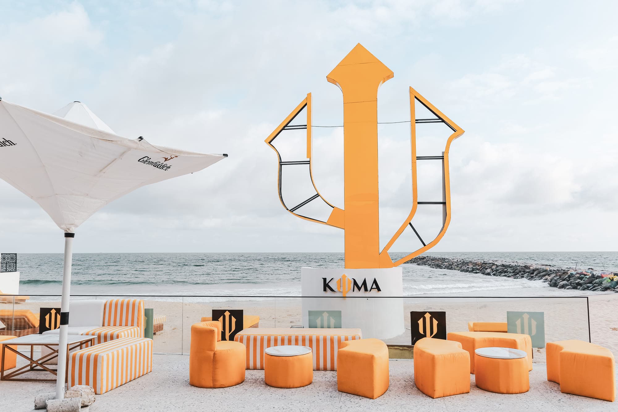 Kyma Beach — the trident sculpture above striped lounge seating, with the sea beyond